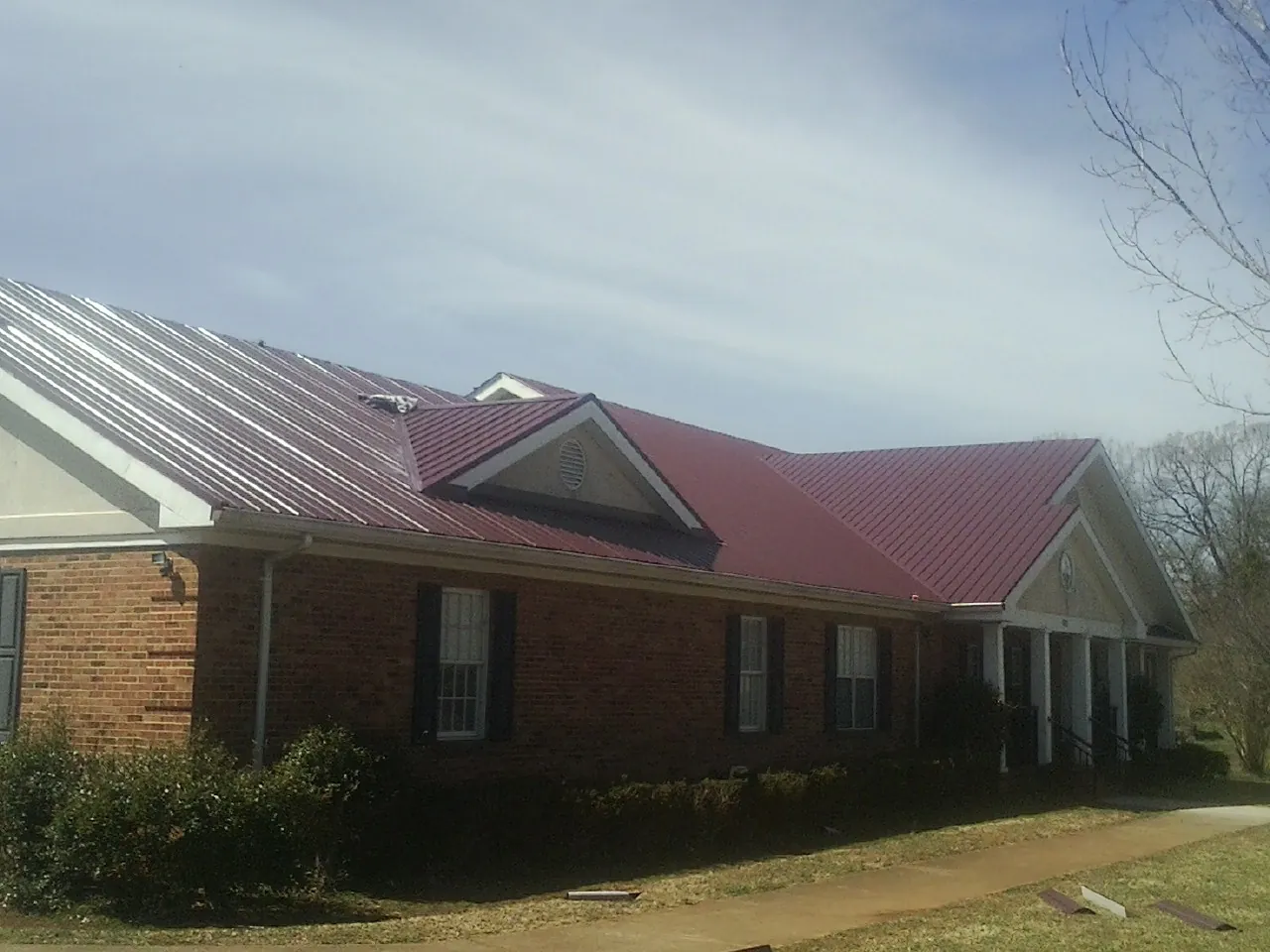 Red metal roof with gabled entries on a long brick building, from a Hail Damage Roof Repair job in Blairs Mills