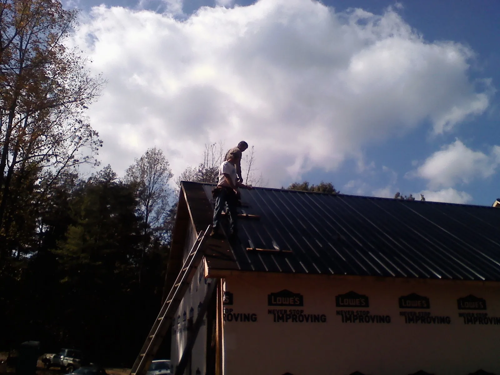 Roofer fastening dark metal panels high against a cloudy sky, from a Roof Inspection job in Blairs Mills