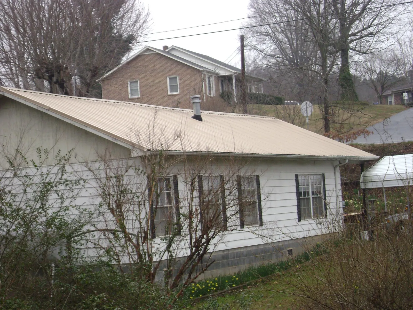 Tan metal roof on a white sided house set into a hillside — Commercial Roofing by Roofing Brothers in Blairs Mills